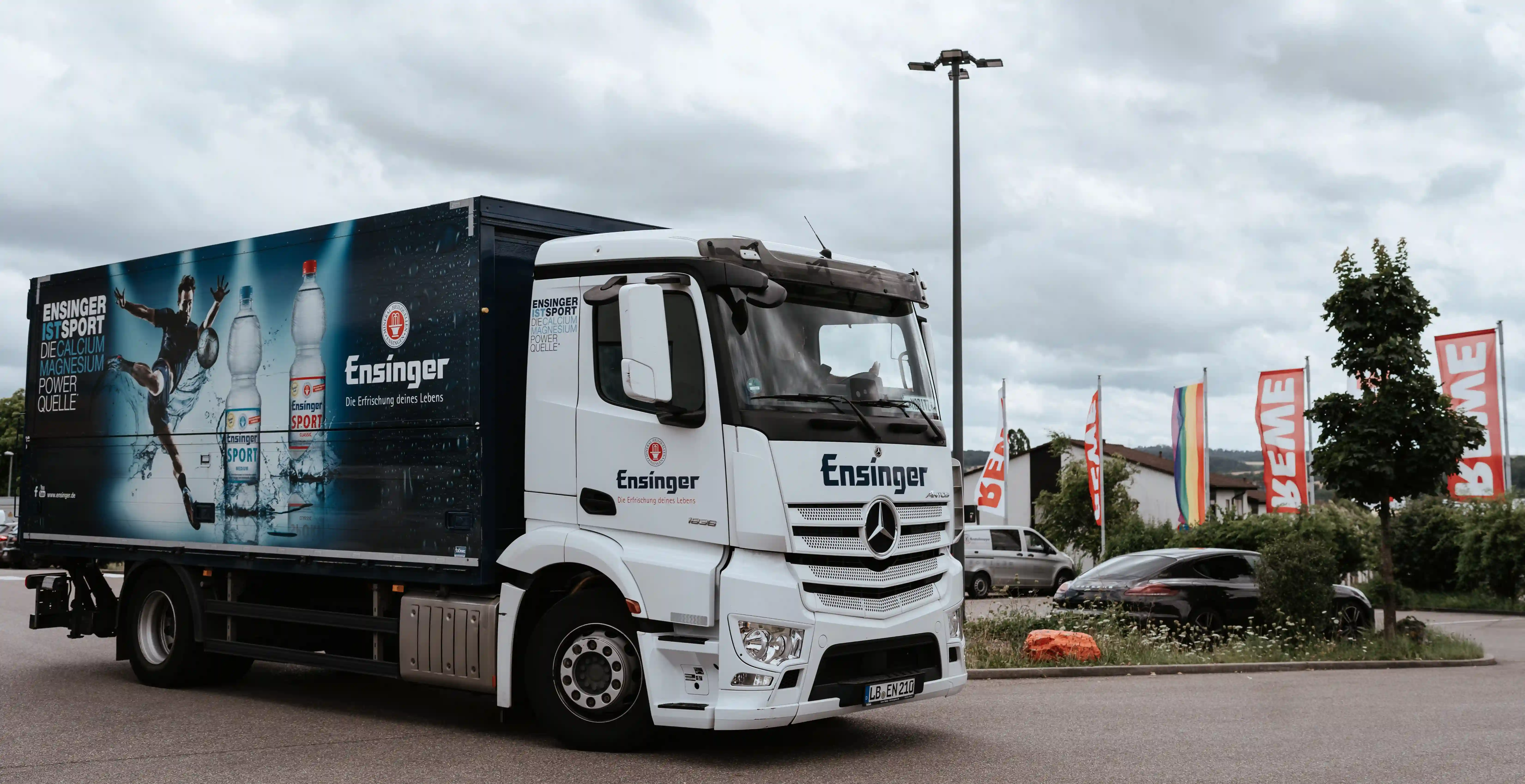 Ensinger%20Lkw%20f%FCr%20Getr%E4nkelogistik%20im%20Au%DFenbereich%20mit%20Werbegrafiken%20auf%20dem%20Auflieger%2C%20die%20Flaschenprodukte%20zeigen%20und%20den%20Getr%E4nketransport%20darstellen.